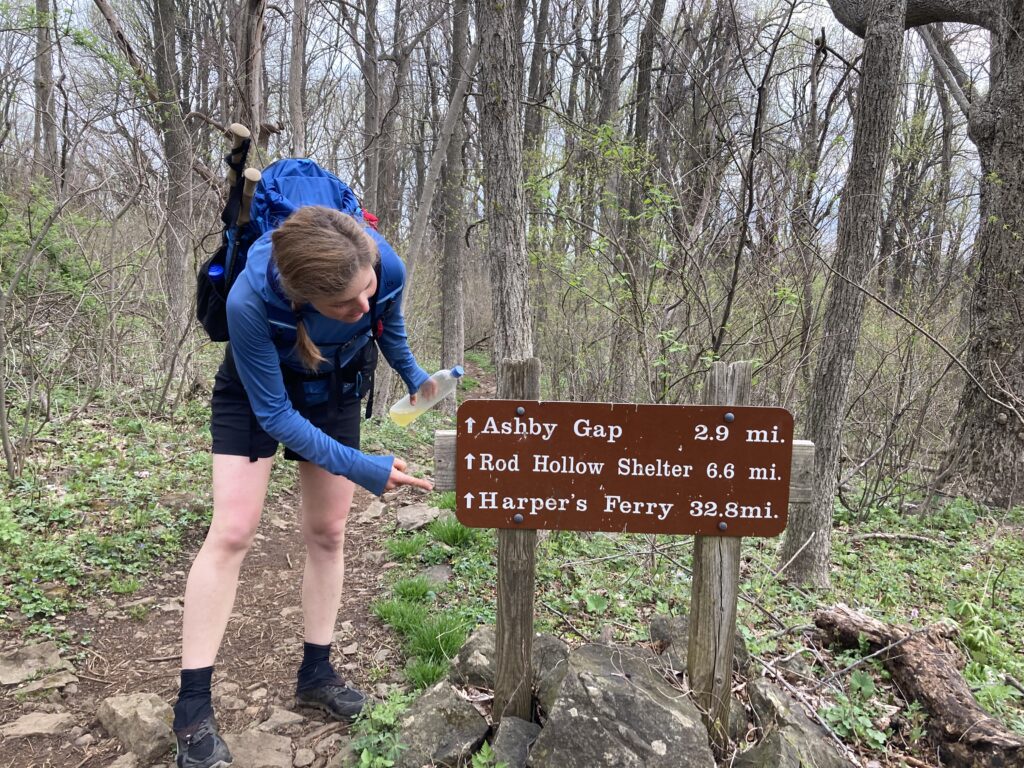 Carolyn posing next to a sign on the Appalachian Trail pointing towards Harpers Ferry