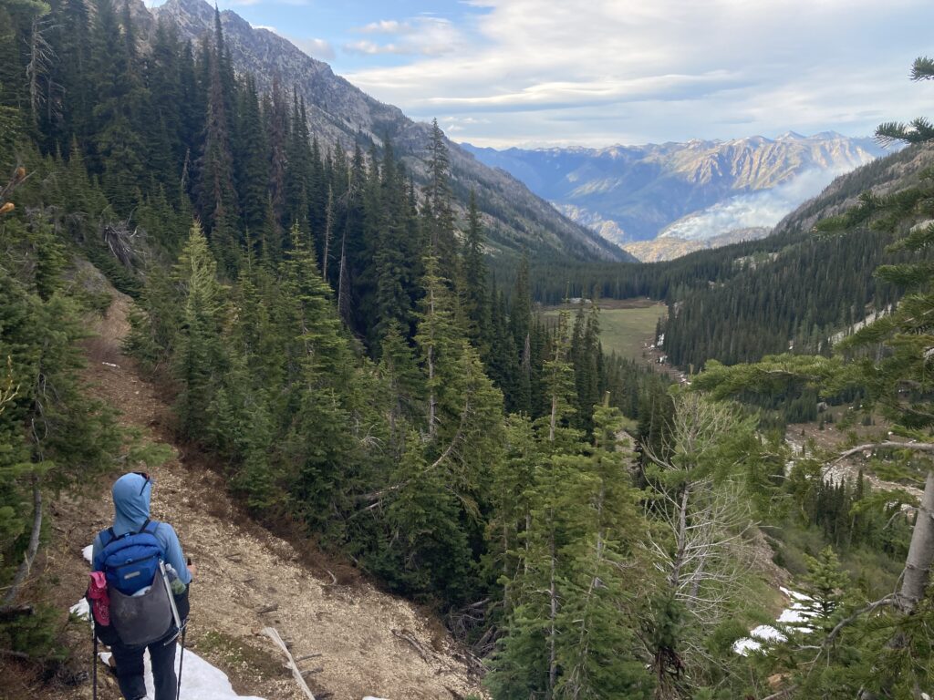 Carolyn hiking down into Emerald Park with fire smoke in the distance in Lake Chelan
