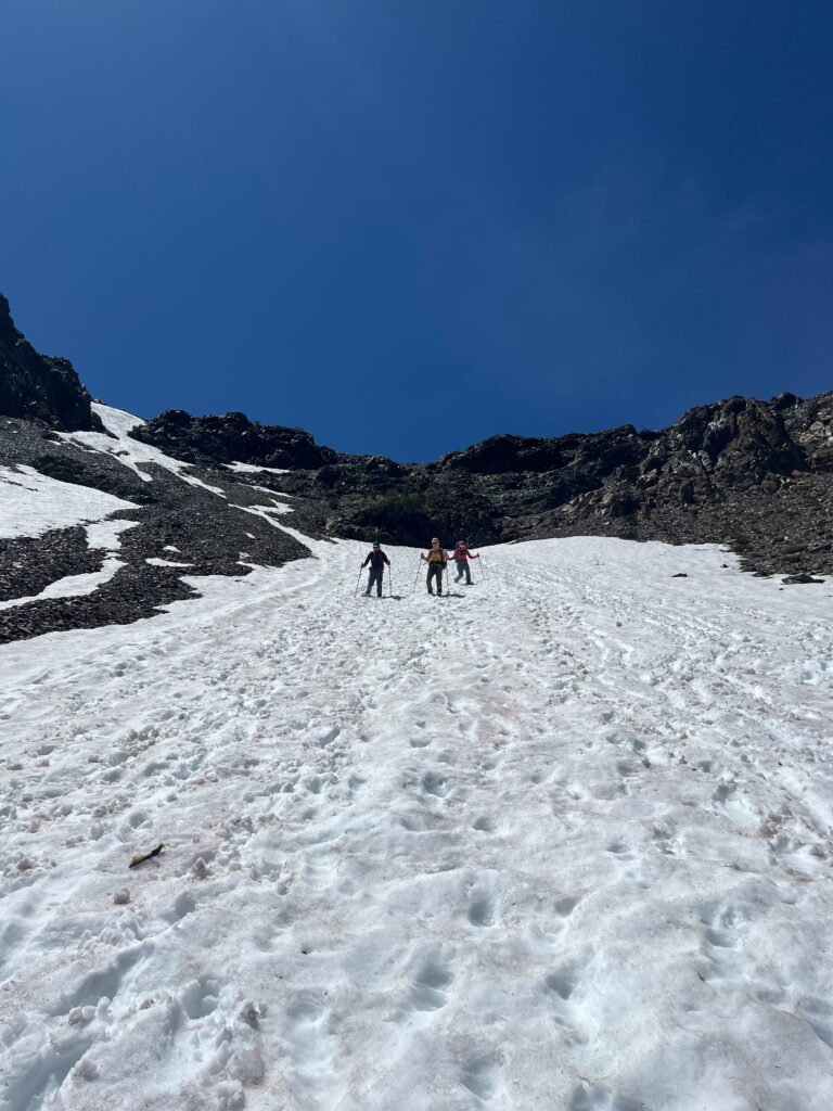 Hikers walking down snow off of Long's Pass in the Alpine Lakes Wilderness