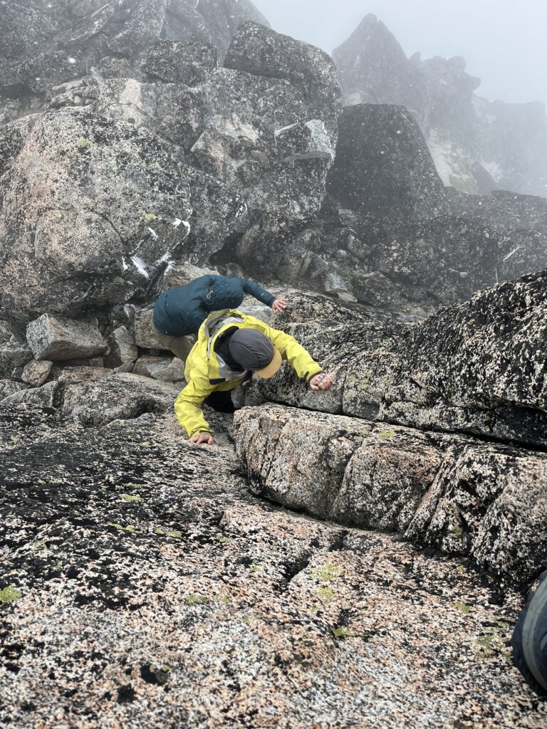 Hikers scarmbling down the summit block of Enchantment Peak in Washington State