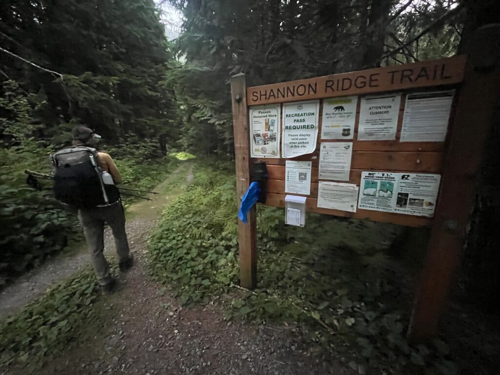 Carolyn hiking by the trailhead sign at the Shannon Ridge trailhead heading towards Mt. Shuksan