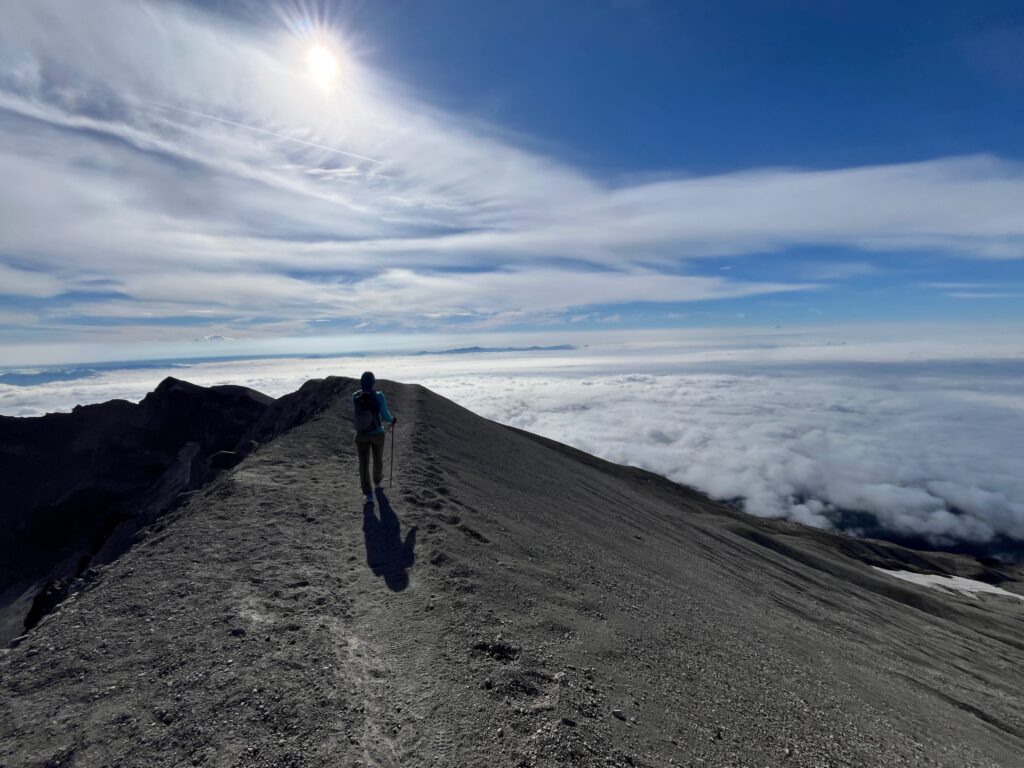 Carolyn walking down from the summit of Mount St. Helens with a view of beautiful clouds